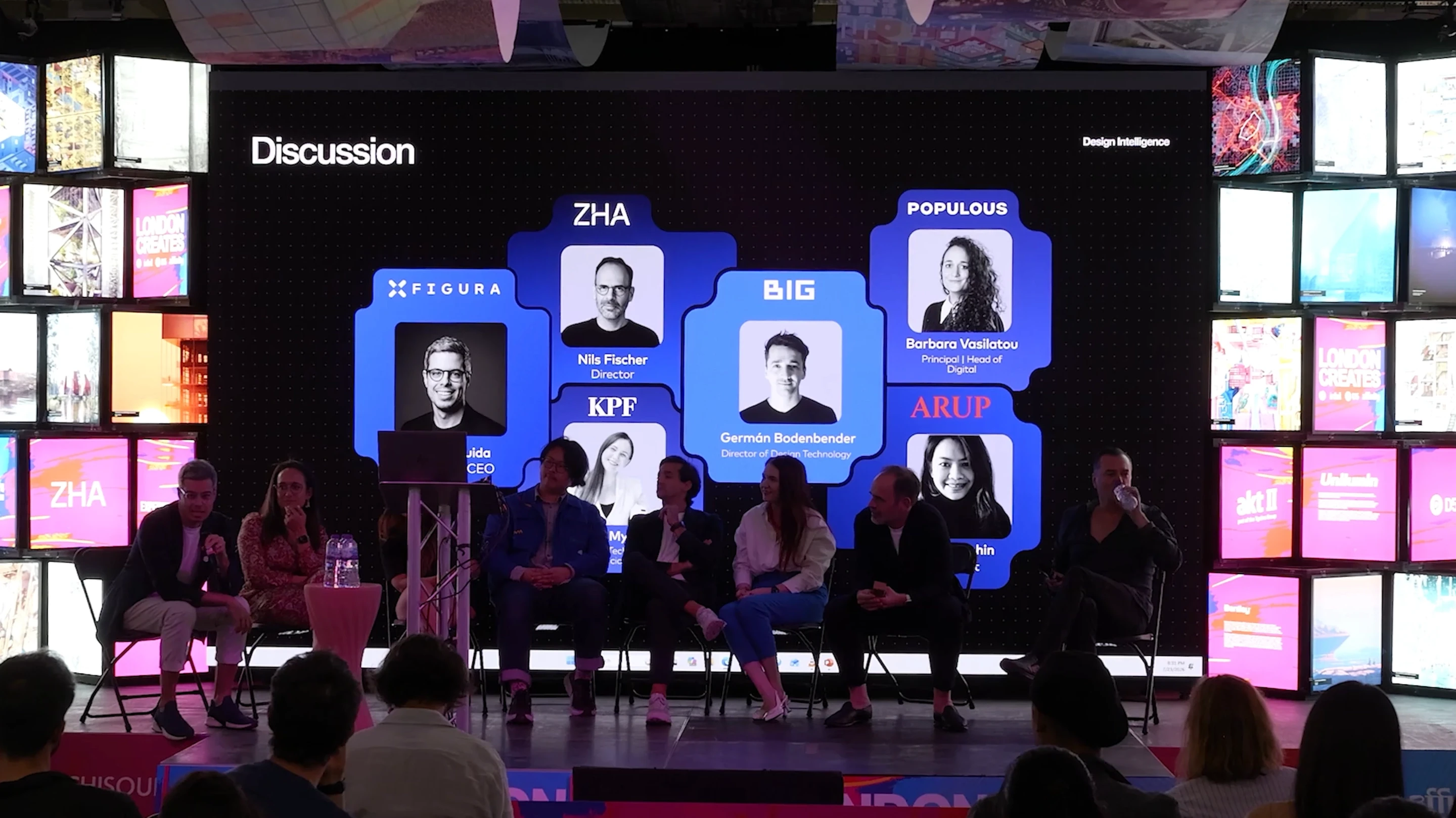A panel discussion on stage with participants seated in front of a large screen displaying designer profiles and logos including ZHA, Figura, KPF, Big, Populous, and Arup.