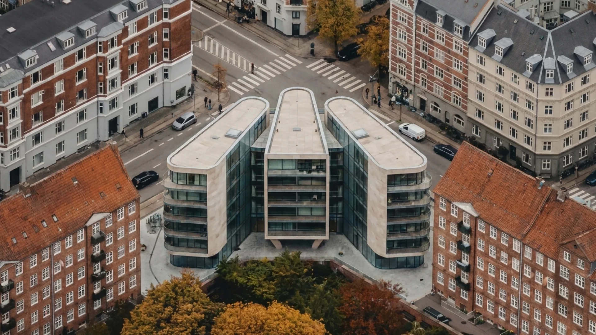 Aerial render — the three-winged building on its corner site, wings splayed to the crossing